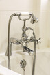 Set of Victorian style chrome finish, deck mounted, bath taps with shower resting in a cradle with tiled wall behind
