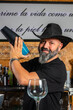 © Rafa - hombre barman con gorro de vaquero preparando un cóctel azul en la barra del bar