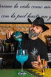 © Rafa - hombre barman con gorro de vaquero preparando un cóctel azul en la barra del bar