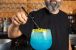 © Rafa - hombre barman con gorro de vaquero preparando un cóctel azul en la barra del bar
