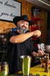 © Rafa - hombre barman con gorro de vaquero preparando un cóctel azul en la barra del bar