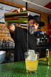 © Rafa - hombre barman con gorro de vaquero preparando un cóctel azul en la barra del bar