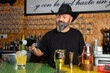 © Rafa - hombre barman con gorro de vaquero preparando un cóctel azul en la barra del bar