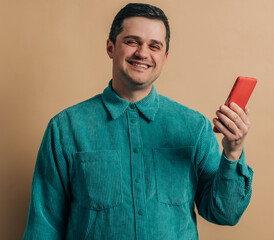 Wall Mural - Stylish caucasian man in green shirt with smartphone on brown background