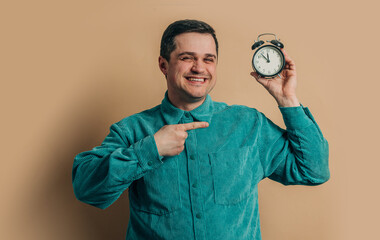 Wall Mural - Stylish caucasian man in green shirt with vintage alarm clock on brown background