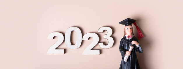 Class of 2023 concept. Wooden number 2023 with graduate statuette on beige background