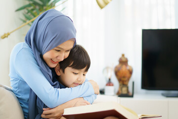 Happy cheerful Asian muslim family stay together in living room in weekend, Beautiful Asian woman muslim and lovely little boy portrait and looking at camera.