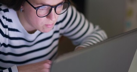 A focused woman in glasses looking at laptop screen with using internet