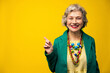 © VISTA by Westend61 - Smiling senior woman pointing against yellow background