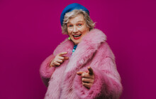 Happy Senior Woman Pink Fur Coat Gesturing Against Colored Background
