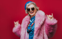 Happy senior woman wearing pink fur coat gesturing against red background