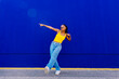 © VISTA by Westend61 - Young woman dancing in front of blue wall