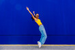© VISTA by Westend61 - Young woman on tiptoes with arms raised by blue wall