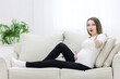 © Andrii - Cute pregnant woman showing thumb up sitting on the sofa