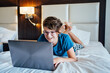 © taniasv - caucasian Teenager Boy Using Laptop In Bed At Home. Laughing at the screen. Wearing glasses. Curly hair. Video call or chat blogging. Coding and studying at home. Gaming