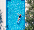 © Soloviova Liudmyla - Sexy young female in black swimsuit bikini, in a straw hat and sunglasses floating on blue waves on inflatable mattress. Olive trees swimming pool. Chill out summer vacation in luxury resorts concept.