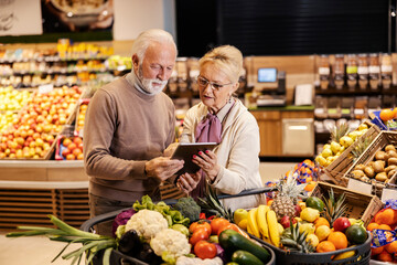 Wall Mural - An old couple is looking at the groceries list on tablet at the supermarket.