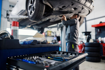 Selective focus on a tools in toolbox at mechanic's shop with mechanic repairing the car in blurry background.