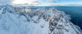 Fototapeta Góry - Snow covered mountain range on coastline in winter, Norway. Senja panoramic aerial view landscape nordic snow cold winter norway ocean cloudy sky snowy mountains. Troms county, Fjordgard 
