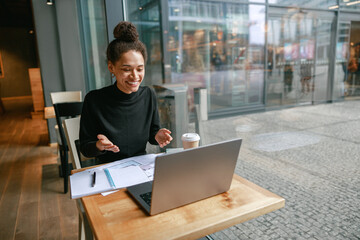 Wall Mural - Woman freelance architect talking with client via video call and discuss project sitting in cafe