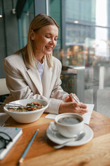 Wall Mural - Attractive businesswoman having lunch and making notes while working in cafe sitting near window