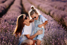 Happy Family In Purple Lavender Field. Young Beautiful Mother And Child Girl Enjoy Walking Blooming Meadow On Summer Day. Mom Having Fun With Pretty Daughter In Nature On Sunset. Mothers Day