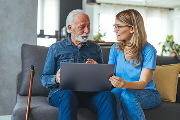 Wall Mural - Female nurse consulting his senior male patient while sitting on sofa during the day. Active senior man using laptop with female carer sitting by on sofa at home.