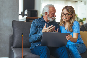 Wall Mural - Female nurse consulting his senior male patient while sitting on sofa during the day. Active senior man using laptop with female carer sitting by on sofa at home. Nurse help senior retirement man 