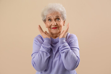 Sticker - Surprised senior woman in lilac sweater on beige background