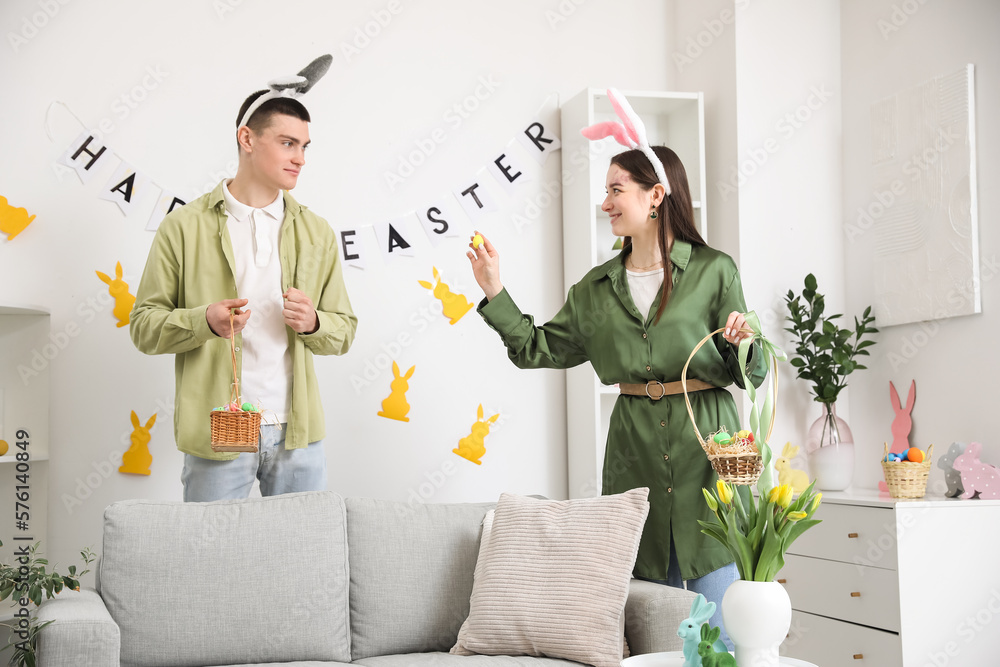 Happy young couple in bunny ears with baskets of Easter eggs at home
