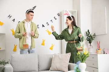 Sticker - Happy young couple in bunny ears with baskets of Easter eggs at home