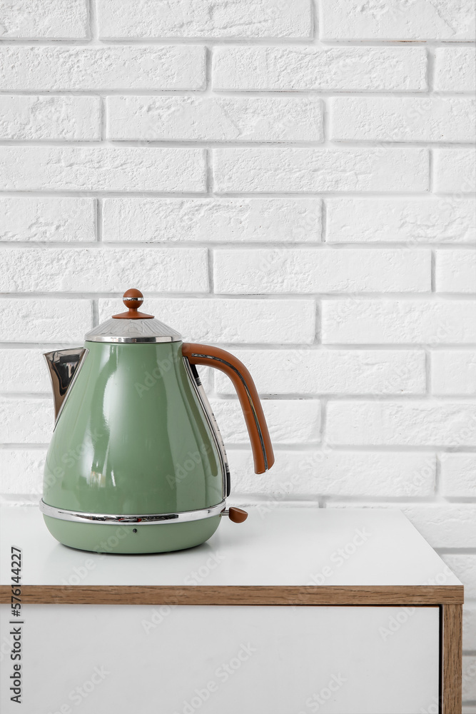 Electric kettle on table near white brick wall