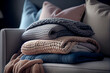 Stack of a variety of soft knit throw blankets and warm sweaters stacked on a grey couch. Generative AI.