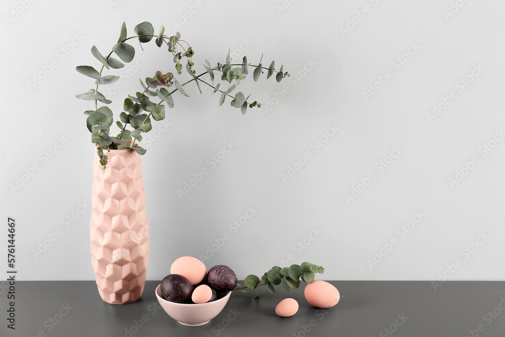 Vase with eucalyptus branches and Easter eggs on table near grey wall
