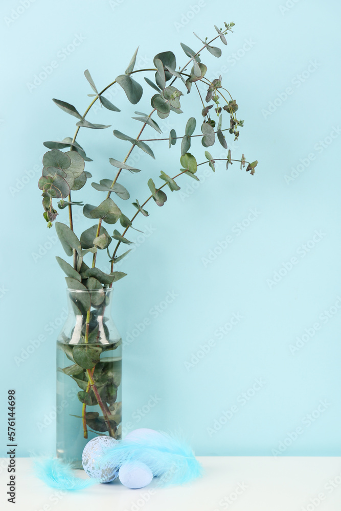 Vase with eucalyptus branches and Easter eggs on table near blue wall