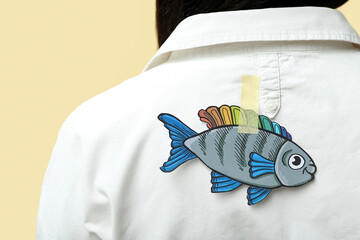 Wall Mural - Paper fish on woman's back against yellow background, closeup. April Fools' Day celebration