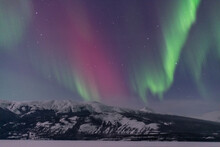 Incredible Aurora Borealis Northern Lights Show Seen In Winter Time Over A Frozen Lake And Snow Capped Mountains. 