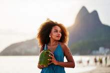 Waist Up Portrait Cheerful Young Brazilian Afro Hairstyle Woman Walking On The Beach Holding A Coconut Water In Ipanema 	