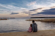 © Kaplitskaya Love - Father and daughter on the shore of the lake watching the sunset sitting on a wooden pier. Lifestyle, leisure, happiness, joy concept. Leisure.
