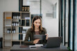 © laddawan - Confident business expert attractive smiling young woman typing laptop ang holding digital tablet  on desk in creative office.