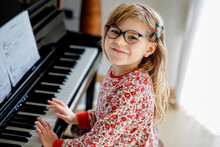 Little Happy Girl Playing Piano In Living Room. Cute Preschool Child With Eye Glasses Having Fun With Learning To Play Music Instrument.