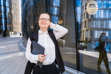 Successful professional woman, in front of a glass building, holding a laptop dressed in business clothes with glasses