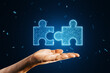 Close up of hand holding glowing digital blue jigsaw puzzle hologram on dark blurry background. Digital solution, collaboration, partners cooperate, implement merge, matching concept.