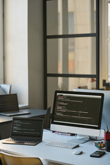 vertical image of computers with codes on the screens standing on workplace of programmer