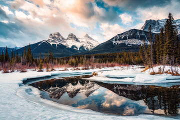 Wall Mural - Three Sisters Mountains with snow covered on bow river reflection in the morning on winter at Canmore