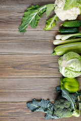 Wall Mural - Border of green raw vegetables on wooden background. Top view of healthy organic food. Copy space