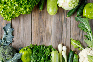 Wall Mural - Frame of green raw vegetables on wooden background. Top view of healthy organic food. Copy space