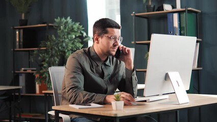 Happy confident business man working on laptop from office talking on mobile. Male programmer executive using computer remote studying, browsing web, having virtual meeting, typing on computer.
