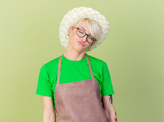 Wall Mural - young gardener woman with short hair in apron and hat looking displeased and annoyed standing over light background