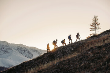 group of tourists silhouettes walks with backpacks in mountains